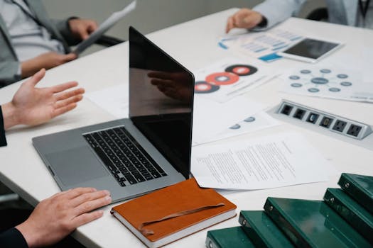 Close-up of a business meeting table with a laptop, documents, and discussion underway.